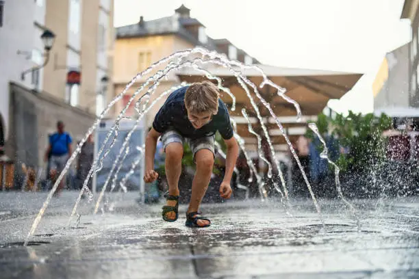 Photo of Little boy running through the public fountain on a street.  Design: Arch. DI Eduard Widmann und Arch. Mag. Erich Wagner