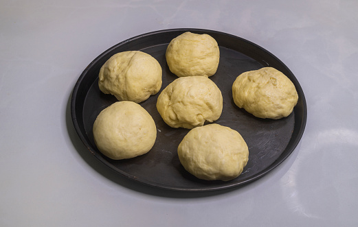 Flour dough balls resting on an oily surface on the round pizza plate. Dough balls have perfectly risen. Hand kneaded the dough for making homemade pastry buns to bake in the oven.