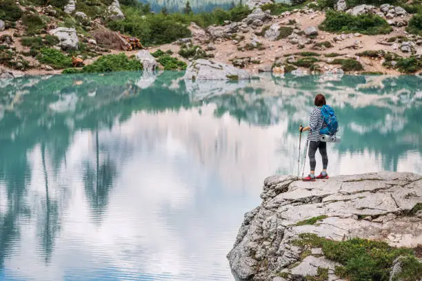 Backpacker woman with backpack and trekking poles enjoying the turquoise Lago di Sorapiss 1925m altitude lake view during mountain walking in Dolomite Mountains, Italy. Active people in nature concept