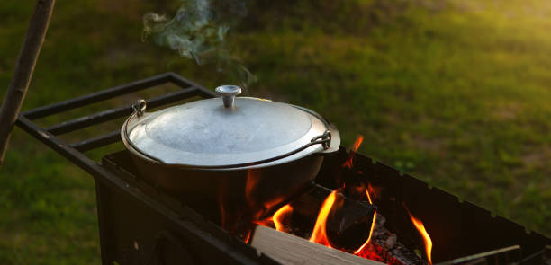 istock A saucepan, cauldron closed with a lid, in a grill on fire, from which steam comes out, on a natural background. Cooking in a pot on the fire. Camping concept. 1331506553