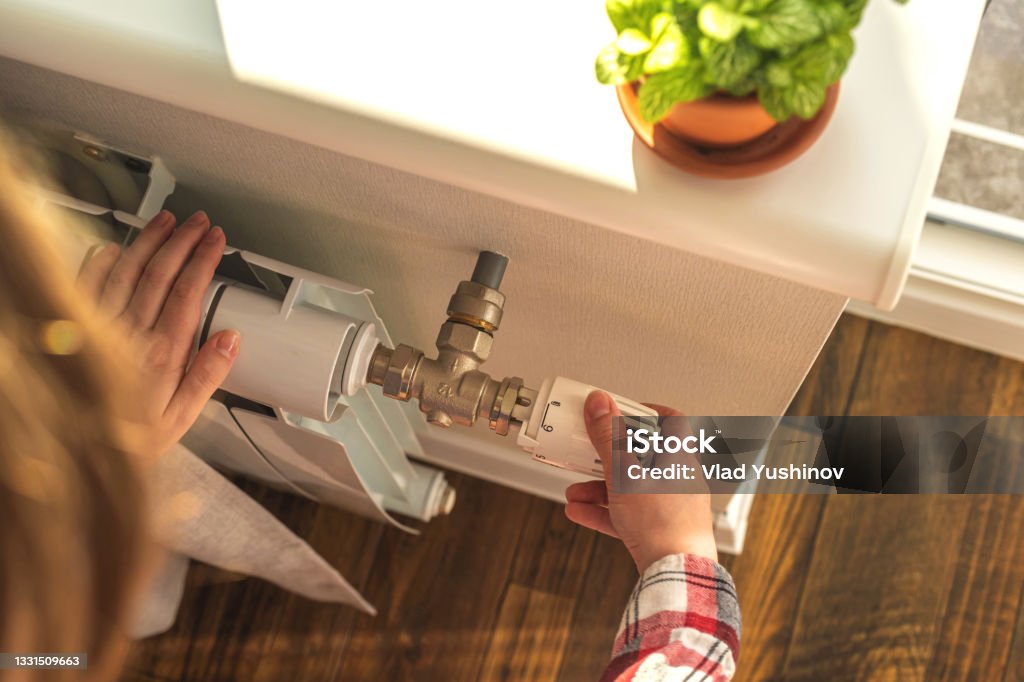 Woman adjusting the temperature on valve of a radiator at home, modern interior background photo Woman adjusting the temperature on valve of a radiator at home, modern interior background Radiator - Heater Stock Photo
