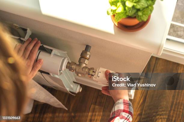 Woman Adjusting The Temperature On Valve Of A Radiator At Home Modern Interior Background Photo Stock Photo - Download Image Now