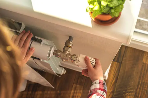 Woman adjusting the temperature on valve of a radiator at home, modern interior background