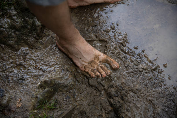 Cropped shot of a woman standing a muddy puddle of water next to her rain boots