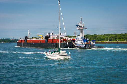 Sandwich, Massachusetts, USA- July 29, 2021- A recreational sailor pilots his luxury sailboat east on the Cape Cod Canal  as he is passed by a motor boat while a large oil tanker heads west after unloading in the port of Boston