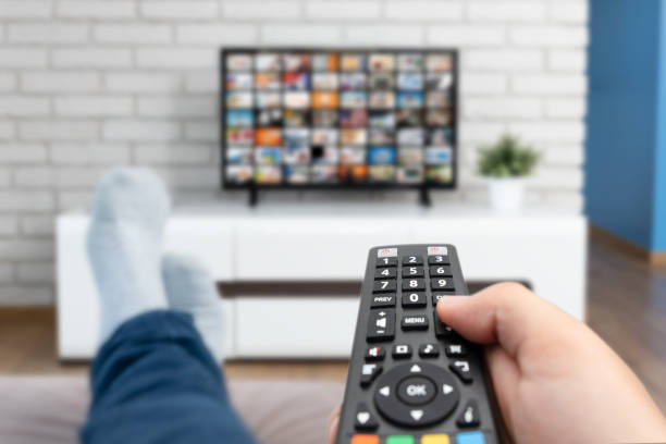 Man watching TV, lying on sofa, legs on table Man watching TV, lying on sofa, legs on table. Person holding remote control in living room part of a series stock pictures, royalty-free photos & images