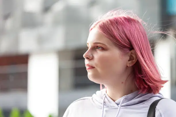 Outdoors portrait of a 20 year old woman in a purple hooded shirt with pink hair
