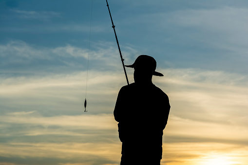 Smiling young man with fishing rod by the sea. Spinning fishing on the sea, the fisherman holds a fishing rod in his hands and turns the reel