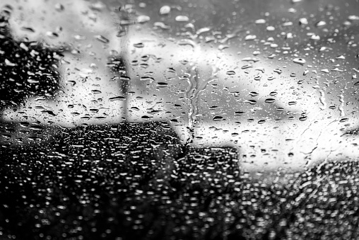 Bokeh, rain, water drops through car glass. Rainy day. Blurred car lanterns. Colored.