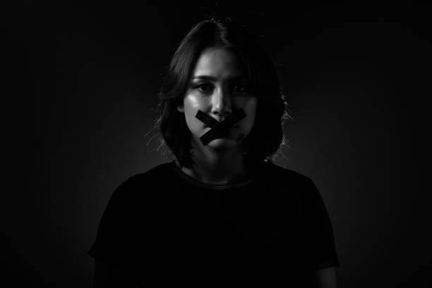 Fashion Beauty Woman has long straight black hair looks at camera Asian Woman feel injustice, insecure and corruption in society So she closes Mouth with duck tape, Concept not to say a word. Dark tone environment copy space closed mouth stock pictures, royalty-free photos & images