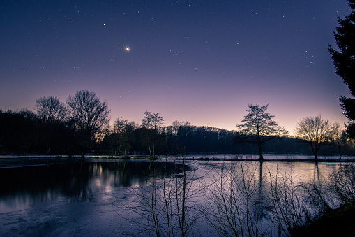 Anochecer en la noche de invierno con estrellas y venus en el cielo nocturno en el paisaje del lago con siluetas árboles y reflexión photo