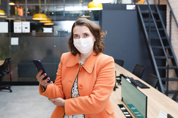 istock Businesswoman using her phone and looking at camera wearing mask 1331541384