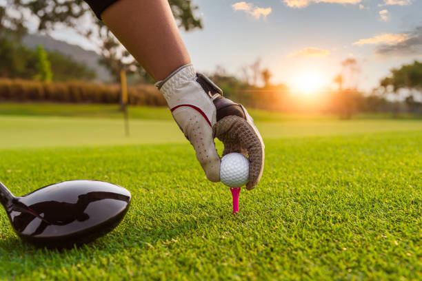 golfer tenir balle de golf mis sur le tee par un gant noir et blanc avec rayon de lumière du soleil flou vert fond de terrain de golf - golf golf club golf swing tee photos et images de collection