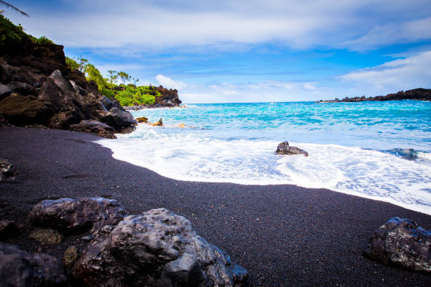 Black Beach, Maui Hawaii Beautiful crystal clear light blue tropical waters lined in dark black sand produced by volcanic rock surrounded by a lush green tropical plants. maui stock pictures, royalty-free photos & images