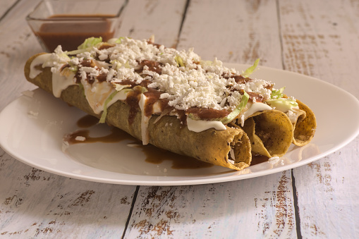 Traditional Mexican food, golden meat tacos (flautas) with red sauce.