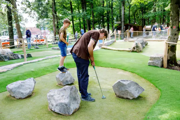 School kid boy playing mini golf with father. Happy child and dad, young man having fun with outdoor activity. Summer sport for children and adults, outdoors. Family vacations or resort