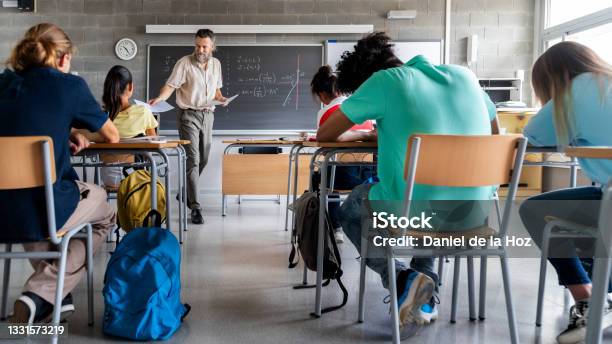 Mature Caucasian Man Teacher Hands Out Exams To Multiracial High School Students Students Ready To Take Exam Stock Photo - Download Image Now