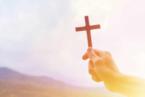 istock Man praying with cross, while holding a crucifix symbol with bright sunbeam on the sky. 1331578309