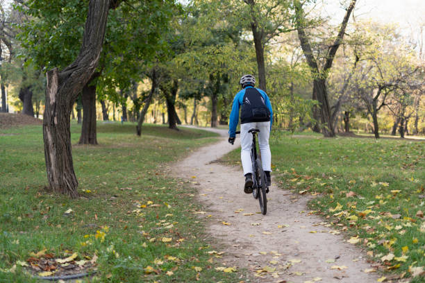 istock A man with a backpack rides a bicycle through the park on a bicycle road. He has a safety helmet and jacket. 1331578337