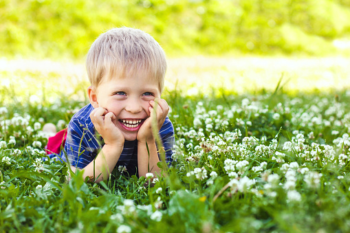 A happy, smiling boy is lying on a green grass lawn. Happy childhood, summer and outdoor recreation