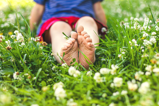 Children's legs of a boy sitting on the green sunny grass, selective focus, soft focus