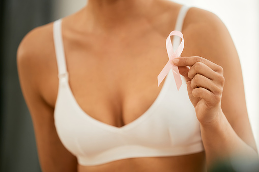 Close-up of woman in bra holding pink breast cancer awareness month ribbon.
