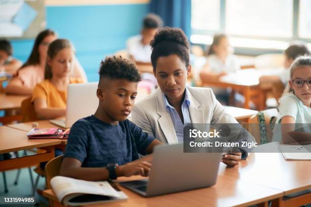 African American Teacher And Her Student Using Laptop During Computer Class At Elementary School Stock Photo - Download Image Now