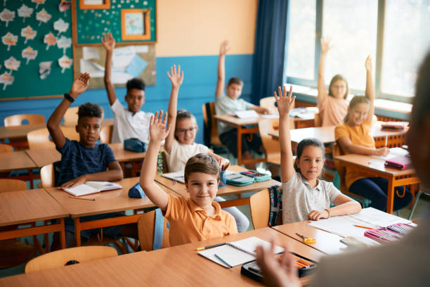 istock Group of happy elementary students raising their hands to answer teacher's question during a class at school. 1331594986