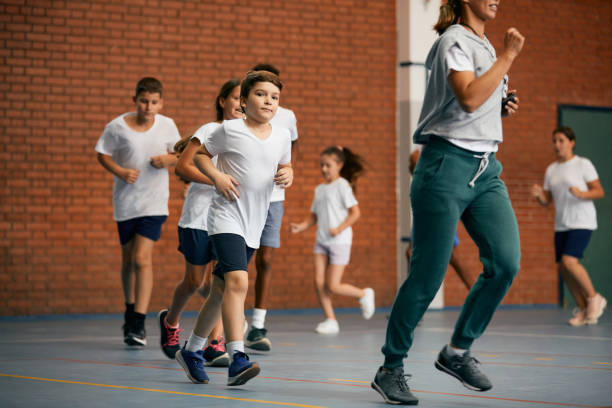 istock Elementary students and their PE teacher running during a class at school gym. 1331594994