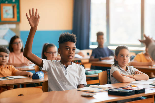istock Black elementary student raising his hand to answer teacher's question in the classroom. 1331595012