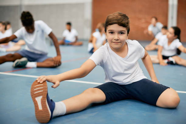 istock Smiling schoolboy stretching his leg on exercise class and looking at camera. 1331595015