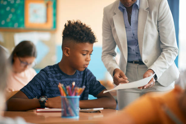 istock Black elementary student learning with help of his teacher during a class at school. 1331595061