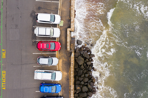 Aerial photograph of a coastal car parking lot or car park taken directly from above as waves break nearby.