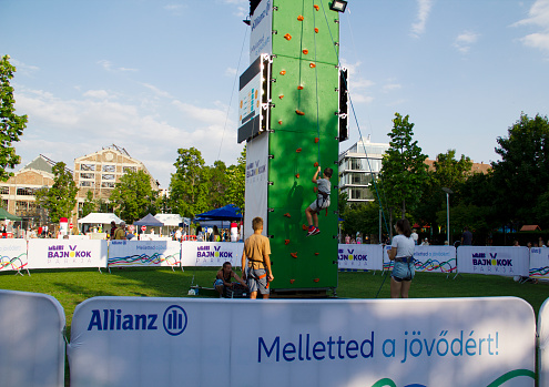 White Caucasian Boy Aged 12-13 Trying Wall Climbing on Cultural and Sport Program Day in Millenaris Public Park in Budapest, Hungary on a Sunny Summer Afternoon in July 2021 - Millenáris Park is a cultural center with community event venues and outdoor recreation facilities in its green parks in 2nd district, Vizivaros on the Buda riverside of Budapest, Hungary.