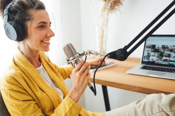 istock Female podcaster recording her podcast using microphone and laptop at his small home broadcast studio. Woman streaming live from homemade radio studio 1331602084