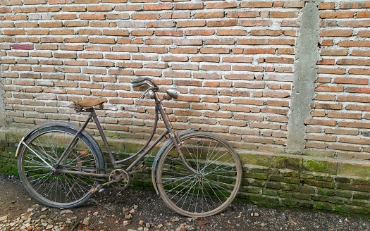Old blue bicycle with metal basket parked beside a beige wall.