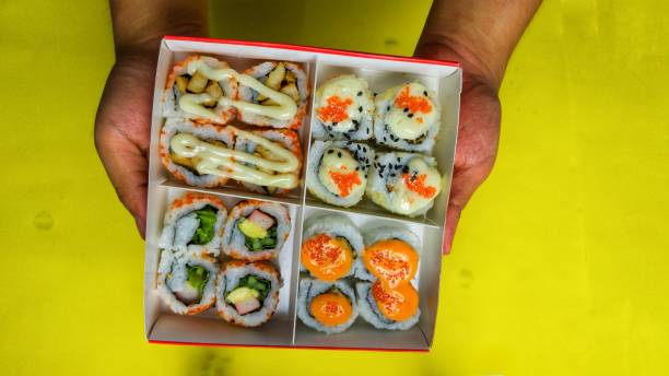 istock box of sushi rolls held by both asian man hands on yellow background 1331604146