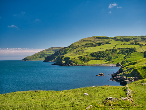 From Torr Head, clear blue water and green hills around the spectacular Antrim Causeway Coast in Northern Ireland, UK - taken on a calm, sunny day in summer with blue sky and blue water.