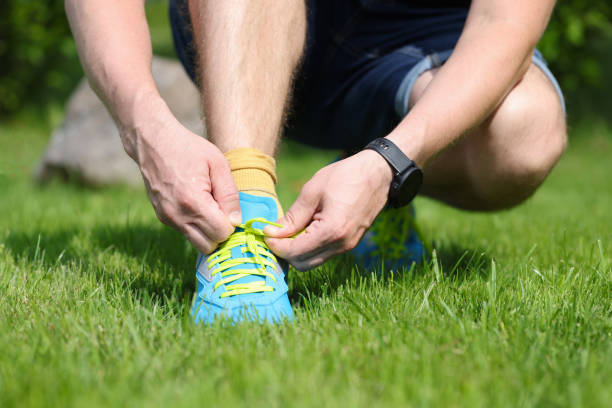 Man is tying laces on bright blue sneakers. Man squatting on the grass in the park concept