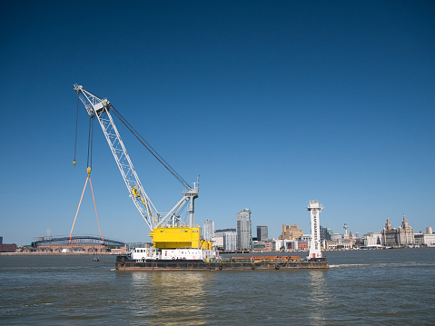 With the Liverpool Mersey waterfront behind, the craneship Lara 1 with electric powered FIGEE offshore 250 tonne crane on a lift to replace the linkspans at Seacombe Ferry.