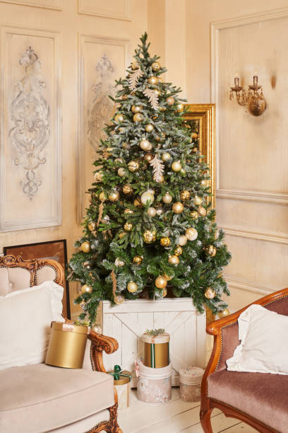 istock a beautiful fluffy tree with slightly snow-covered branches decorated with large golden balls and feather-shaped toys stands in the corner of a room with light walls. there are boxes with gifts under it 1331611476