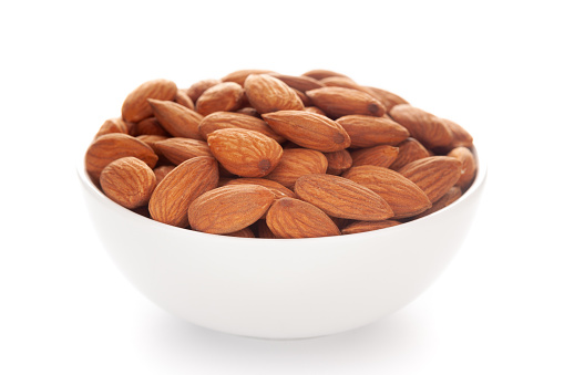 Close-up of brown almonds (Prunus dulcis) kernels in a white ceramic bowl over white background
