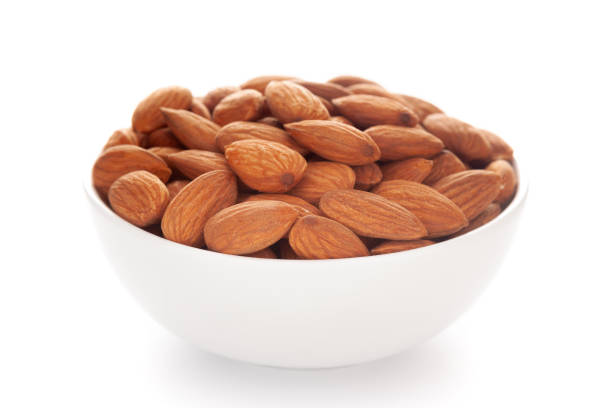 Close-up of brown almonds (Prunus dulcis) kernels in a white ceramic bowl over white background Close-up of brown almonds (Prunus dulcis) kernels in a white ceramic bowl over white background almond tree stock pictures, royalty-free photos & images