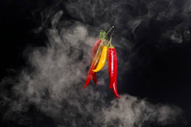 A bunch of spicy peppers in various colors with some smoke against a black backdrop