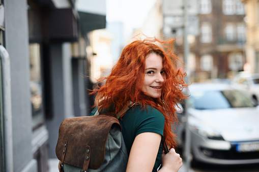 A portrait of young woman with backpack walking outdoors in city, looking at camera.