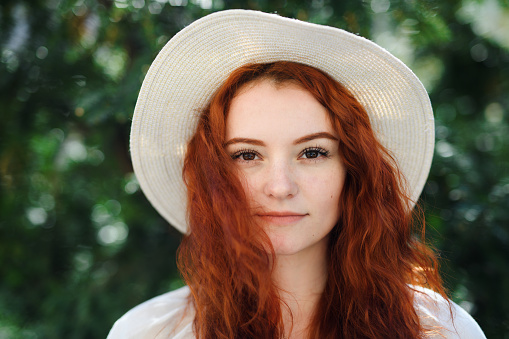 A close-up portrait of young woman with a hat outdoors in city, looking at camera.