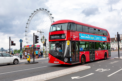 London, England; 07/27/2021: English double-decker bus crossing westminster bridge with the ferris wheel \
