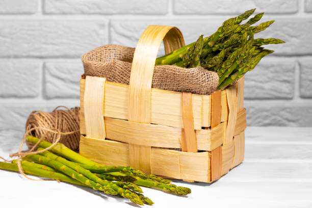 アスパラガス。白い背景に木製のバスケットに新鮮な緑のアスパラガス。健康的な野菜ダイエット。菜食主義。生野菜、市場。ビーガンの背景 - asparagus vegetable market basket ストックフォトと画像