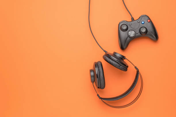 istock Black headphones and a black game console on an orange background. Flat lay. Place for text. 1331633070
