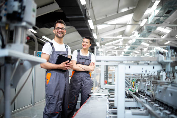 Portrait of production line workers controlling manufacturing process of modern packaging industrial machine in printing factory. Portrait of production line workers controlling manufacturing process of modern packaging industrial machine in printing factory. production line worker stock pictures, royalty-free photos & images